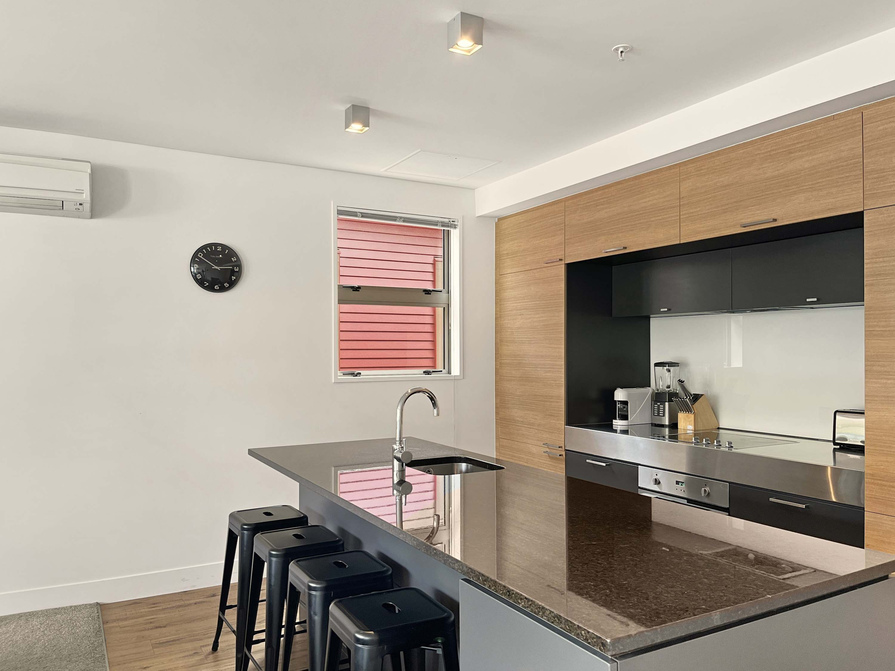 Una cocina moderna con una isla central, taburetes de bar, horno empotrado y cafetera.