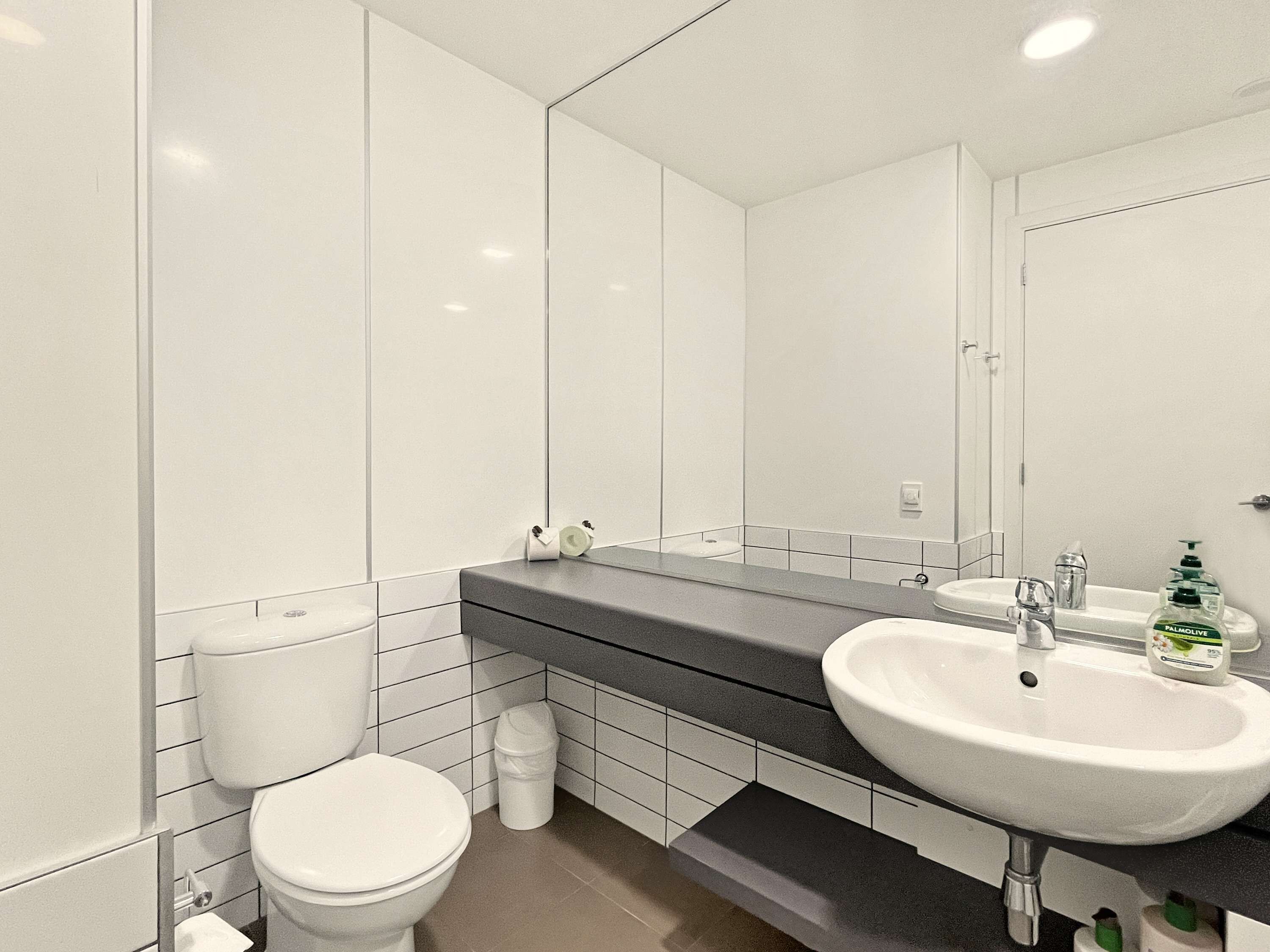 A modern bathroom with a white toilet, a sink with a mirror above it, and a trash bin.