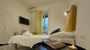 A hotel room with a bed, a bedside table with a book and a candle, a TV mounted on the wall, and a window with curtains. - Terrace Boutuque inn (Rome)