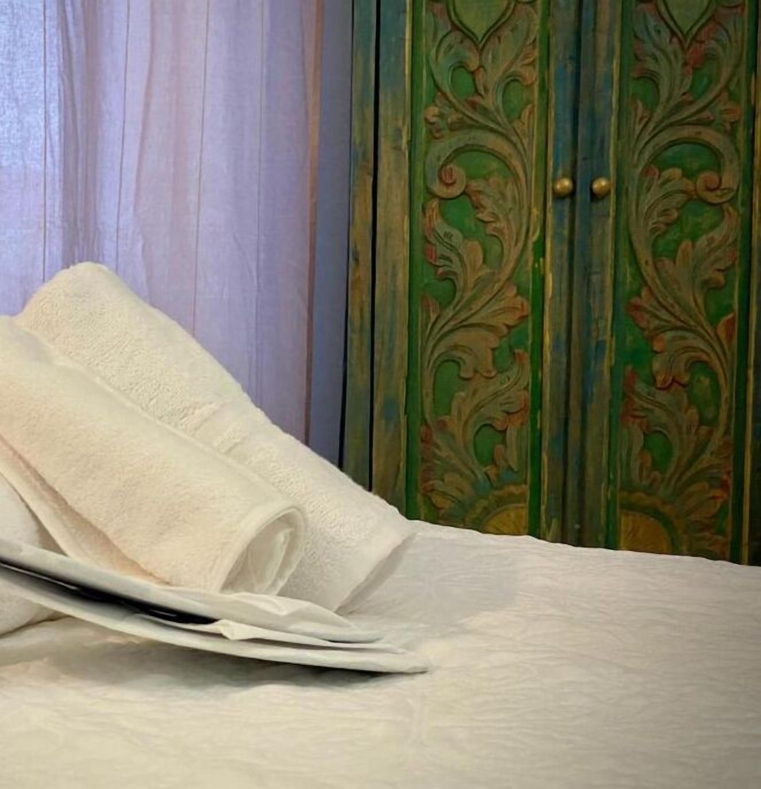 Una toalla blanca doblada con cuidado sobre una cama con cabecera de madera y una puerta verde con detalles ornamentales.