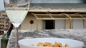 Una copa de vino blanco sobre una mesa con un cuenco de cacahuates y algunas flores rosadas.