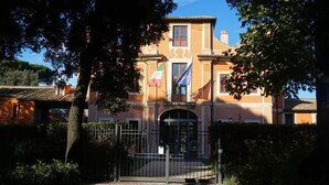 A two-story building with a gated entrance, a flagpole with the Italian flag, and a clear sky. - Terrace Boutuque inn (Rome)