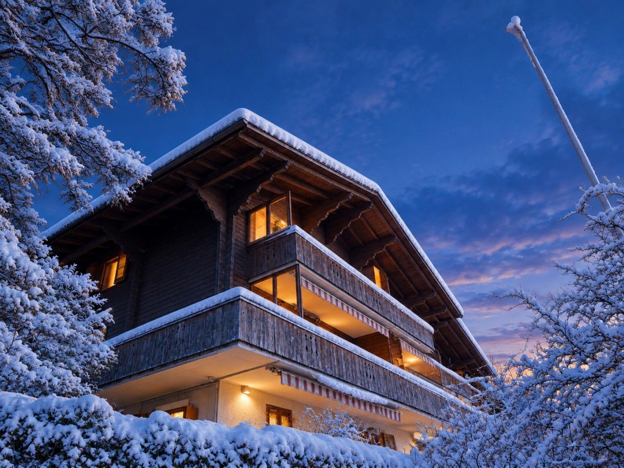 Un chalet en bois à plusieurs étages, doté de balcons et entouré d’arbres couverts de neige.
