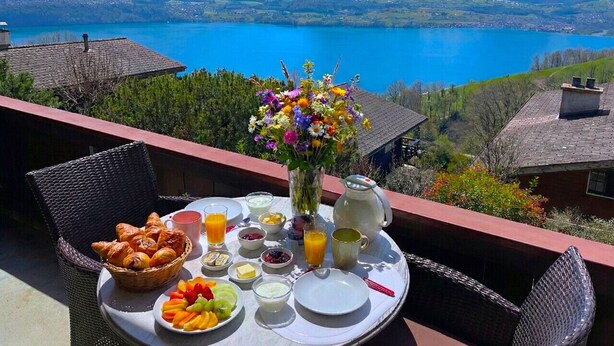 Un coin petit-déjeuner aménagé sur un balcon donnant sur un lac de montagne, avec des sommets enneigés en toile de fond.