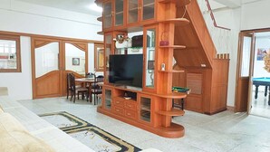 Un vaste salon agrémenté d’un meuble de rangement en bois pour les appareils multimédias, un coin repas avec une table et des chaises, et un escalier menant à l’étage supérieur.