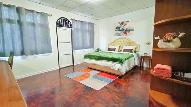 Une chambre à coucher comprenant un lit, une table de chevet, une étagère avec des objets décoratifs, une fenêtre avec des rideaux et une porte.