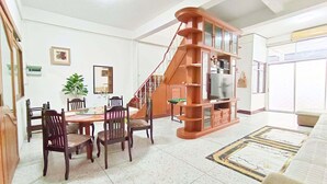 Un salon spacieux comprenant un coin repas, un escalier et une grande bibliothèque.
