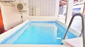 Une piscine rectangulaire avec un bord carrelé, une échelle en métal et un climatiseur fixé au mur.