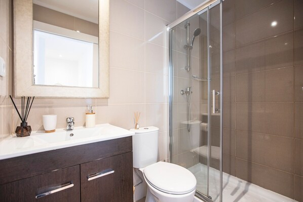 A modern bathroom with a glass shower enclosure, a white toilet, and a vanity with a mirror.
