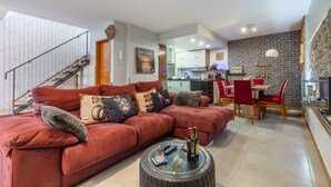 A modern living room with a sectional sofa, a coffee table, and a dining area with red chairs. - FLH Funchal Sissi Lanço with View (Funchal)