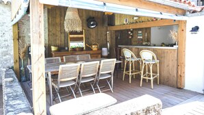 A wooden deck with a table and chairs, a bar area, and a rustic kitchen setup. - Exceptional house in Nieul-sur-Mer (Nieul-sur-Mer)