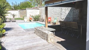 A wooden deck with a stone wall, a pool, and outdoor furniture. - Exceptional house in Nieul-sur-Mer (Nieul-sur-Mer)