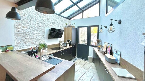 A modern kitchen with a stone wall, a large island, and a skylight. - Exceptional house in Nieul-sur-Mer (Nieul-sur-Mer)