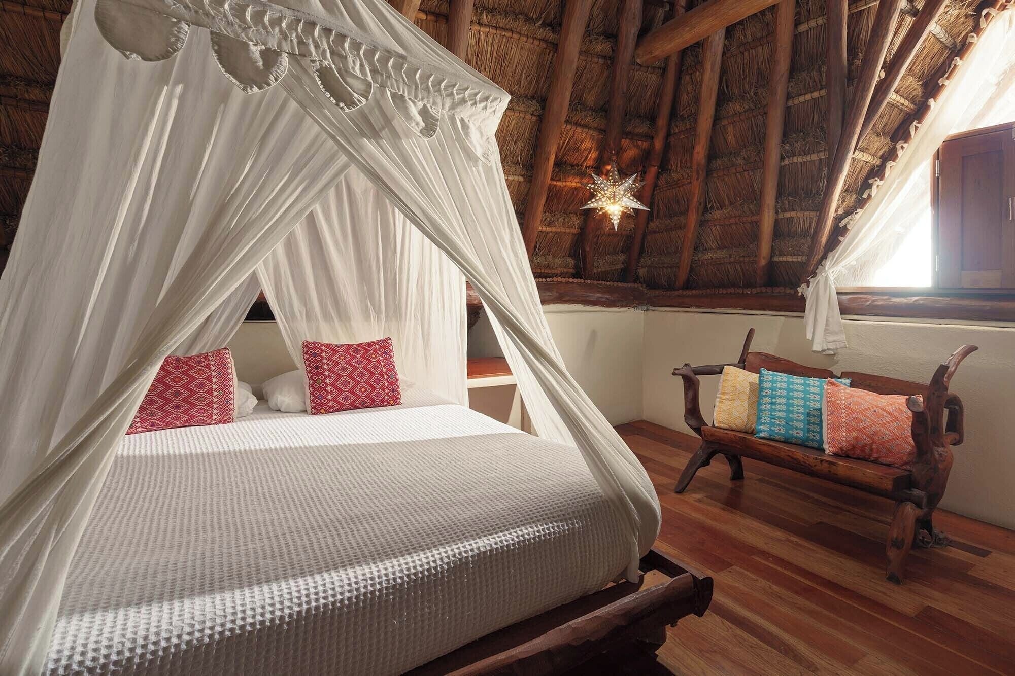 A room with a canopy bed, wooden bench with cushions, and a star-shaped hanging light.