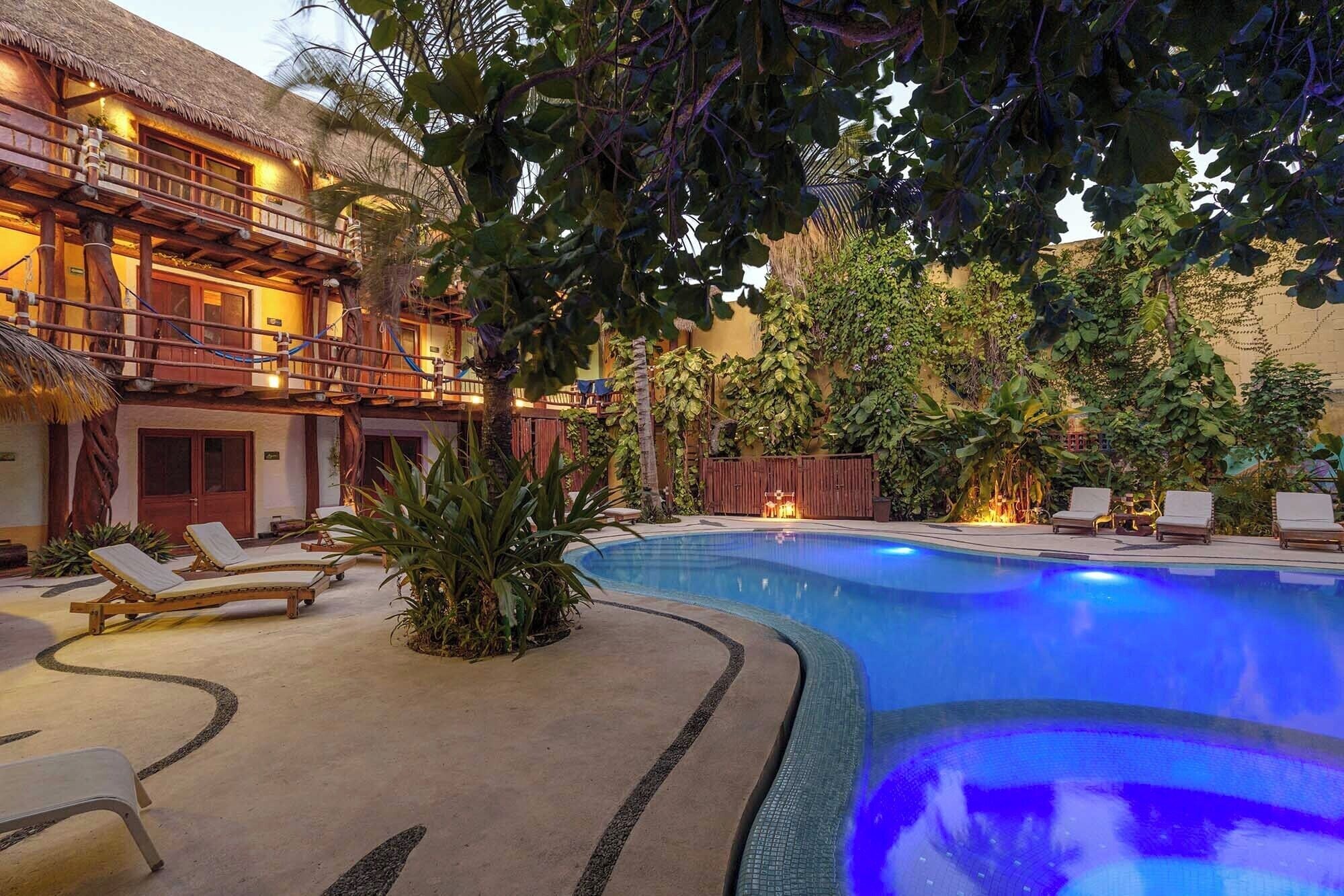 A swimming pool with lounge chairs, a thatched-roof building, and lush greenery.