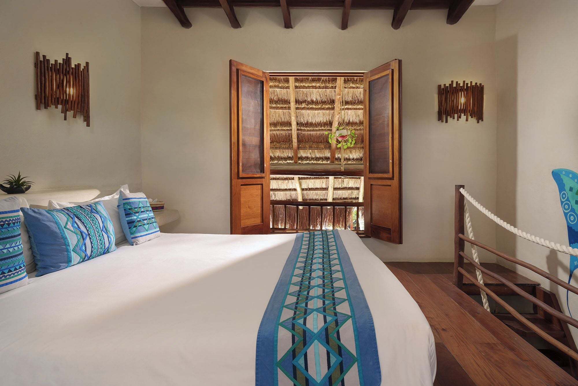 A bedroom with a large bed, a wooden window frame, and a rope barrier.