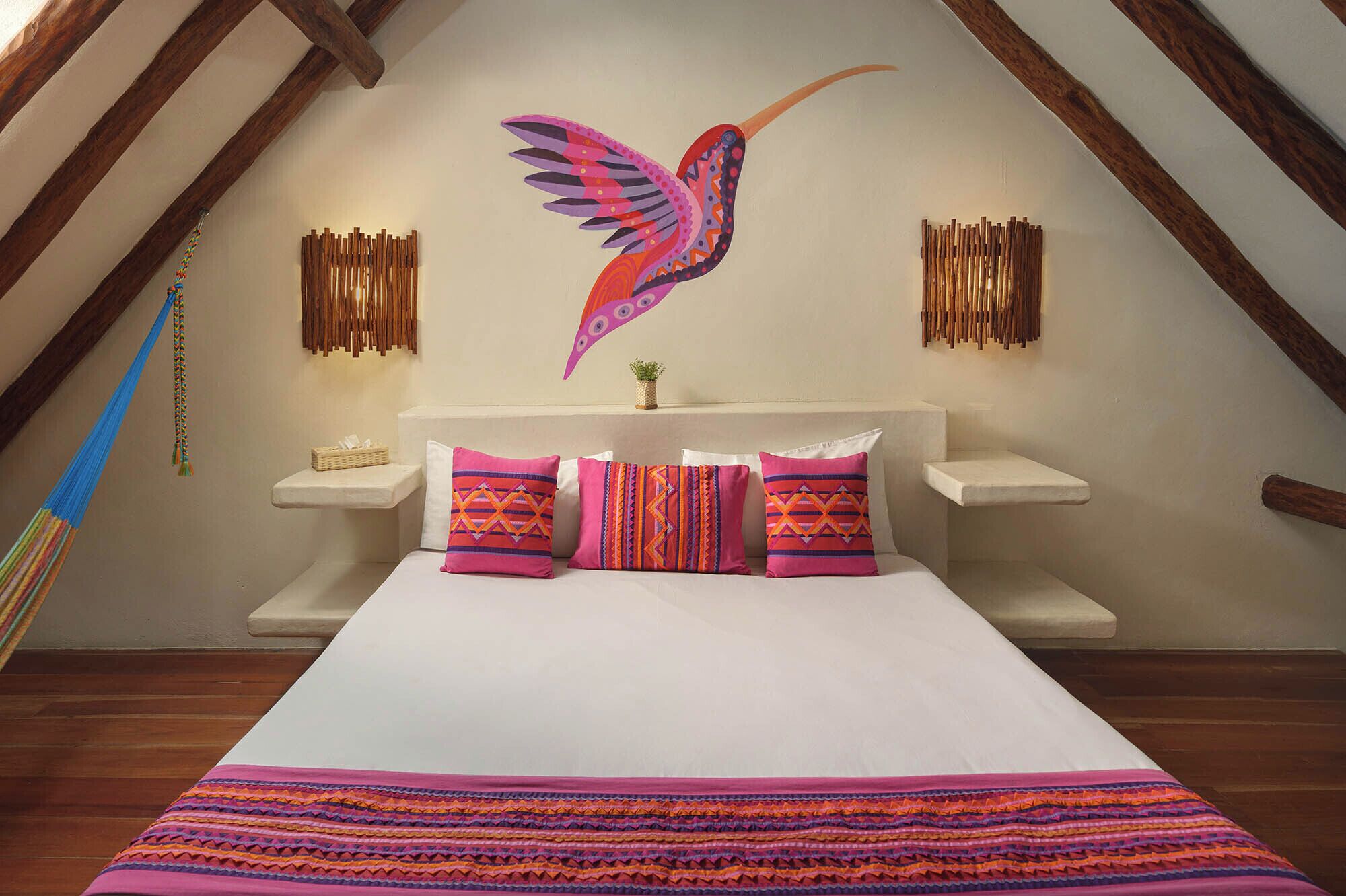 A bedroom with a large bed, colorful pillows, a wall-mounted artwork of a bird, and wooden wall decor.