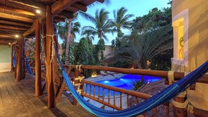 Une terrasse en bois avec un hamac, une piscine et des palmiers.