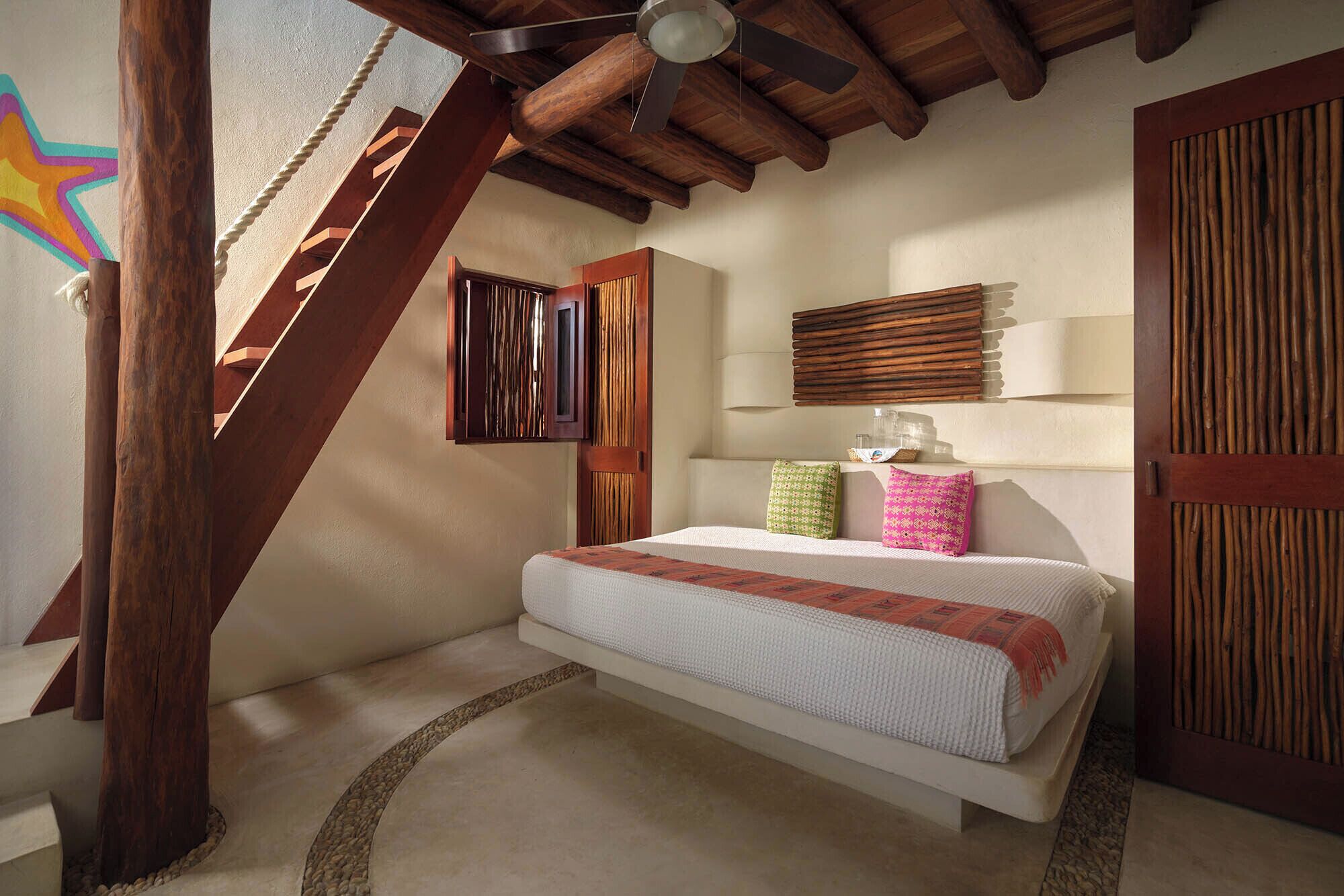 A bedroom with a bed, wooden beams, a sloped ceiling, and a star mural on the wall.