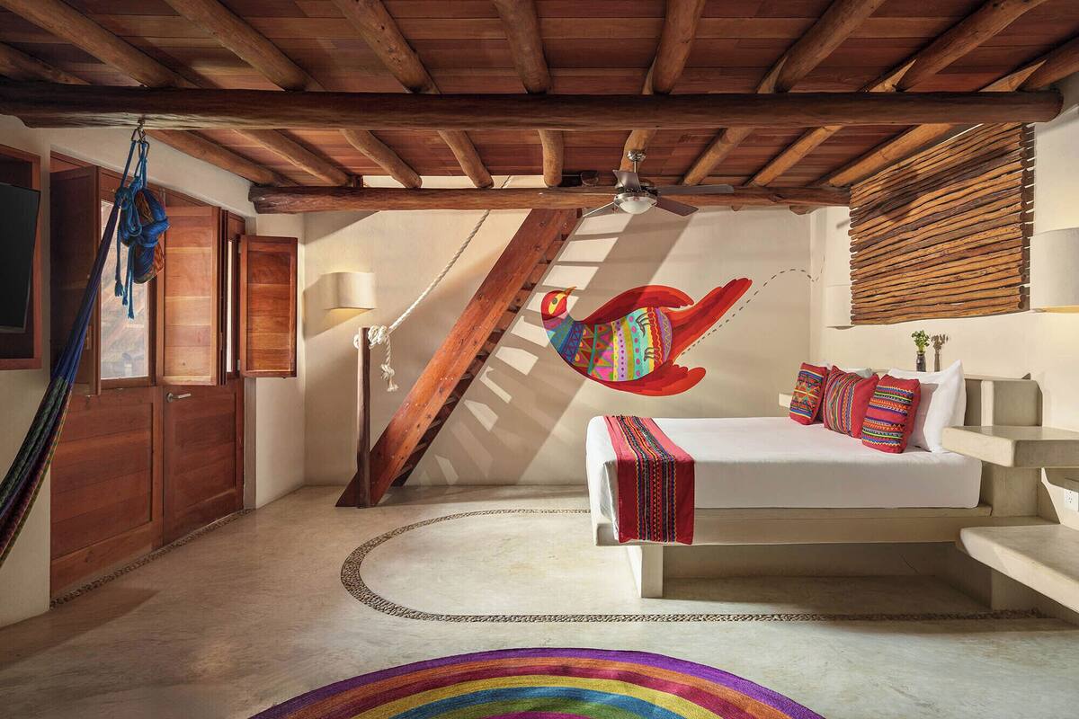 Une chambre à coucher avec un lit, une table de chevet, une lampe, un ventilateur de plafond, un hamac et un tapis coloré.