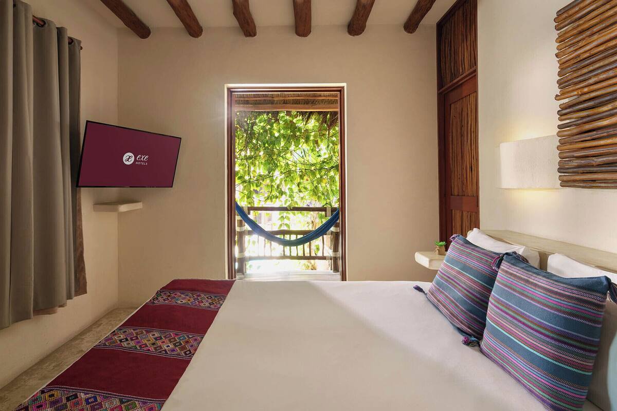 Une chambre d’hôtel avec un lit, un téléviseur fixé au mur, un hamac et une vue sur la verdure.