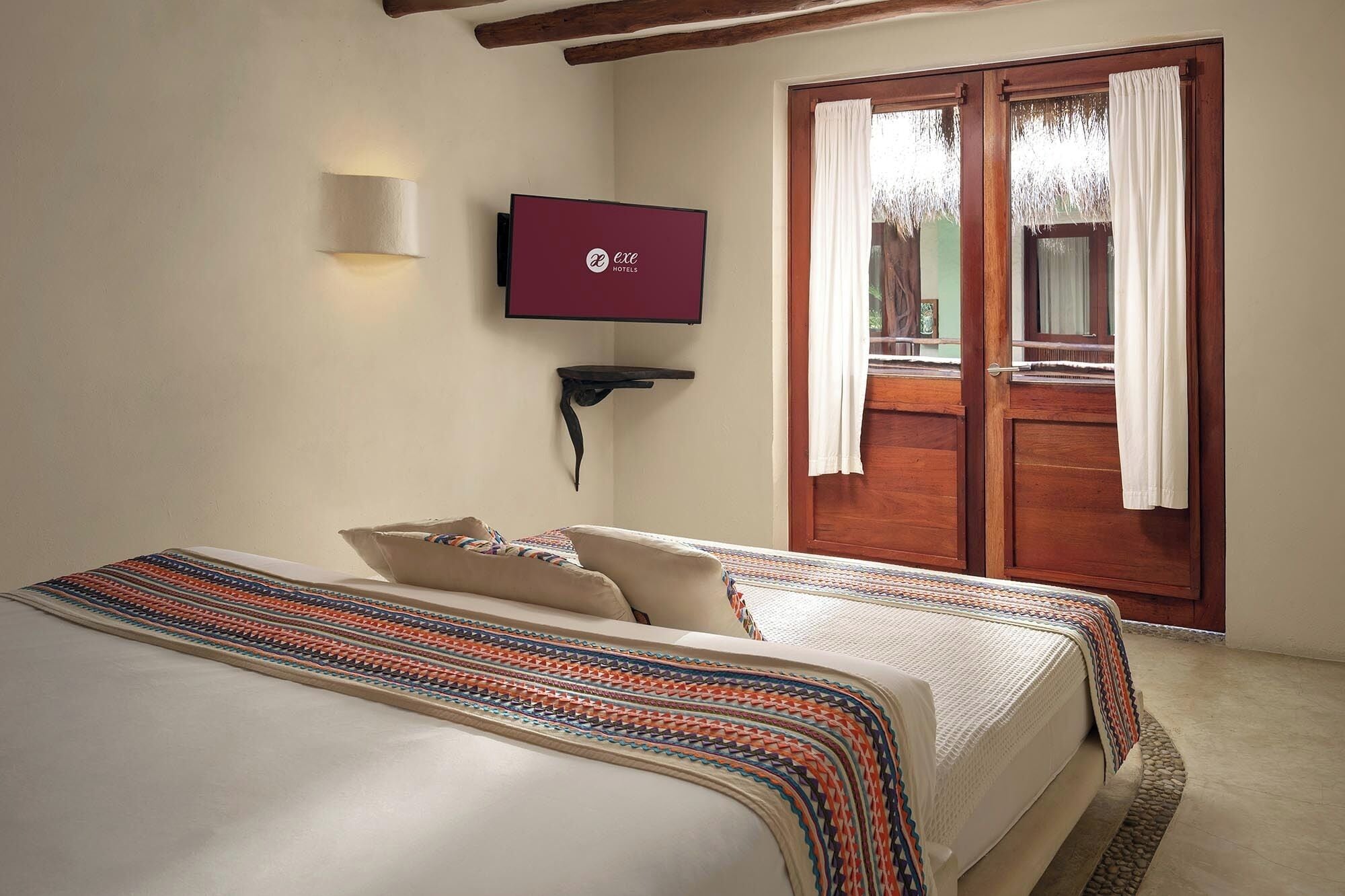 A bedroom with a bed, a TV mounted on the wall, and a sliding glass door leading to an outdoor area.