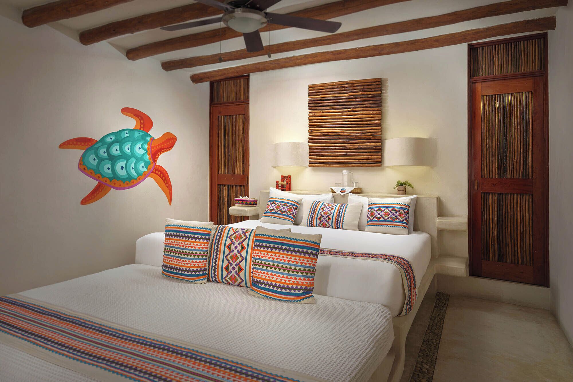 A hotel room with a bed, pillows, a wall mural, a ceiling fan, and wooden paneling.