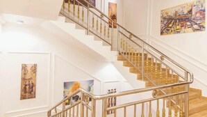 Eine Treppe mit Metallgeländer und Holzstufen, begrenzt von weißen Wänden und gerahmten Kunstwerken.