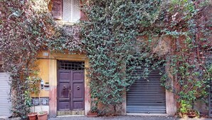 Un edificio con una puerta de madera cerrada y un portón de garaje con contraventanas, rodeado de hiedra densa.