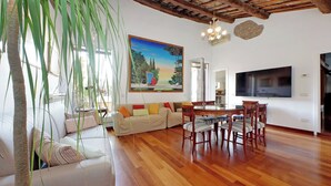 Una sala de estar con techo de madera, un sofá con cojines de colores, una mesa de comedor con sillas y un cuadro en la pared.