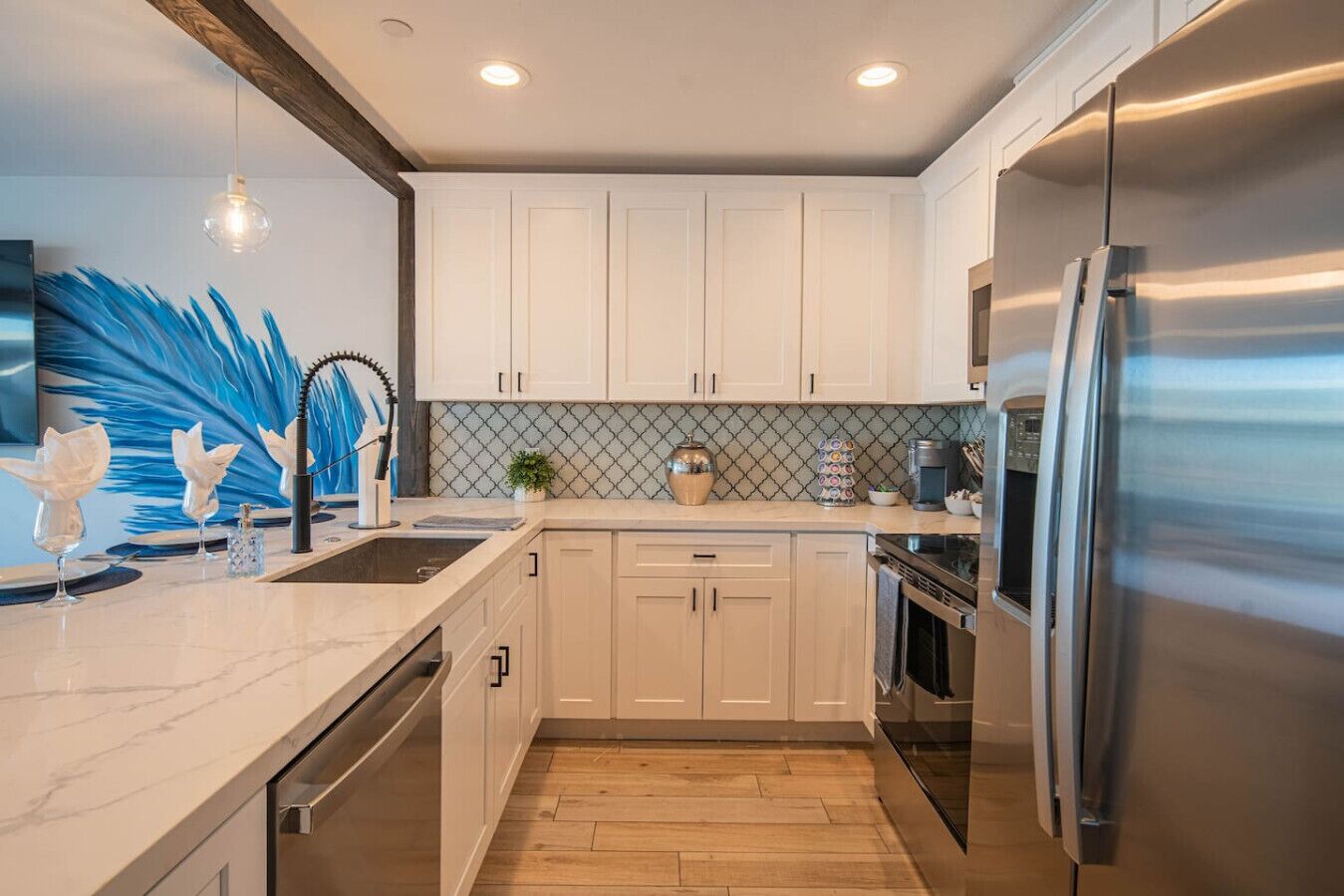 A modern kitchen with white cabinets, a stainless steel refrigerator, a marble countertop, and a wooden floor.