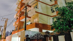 Un edificio residencial de varios pisos con balcones, una entrada con portones y líneas eléctricas visibles.