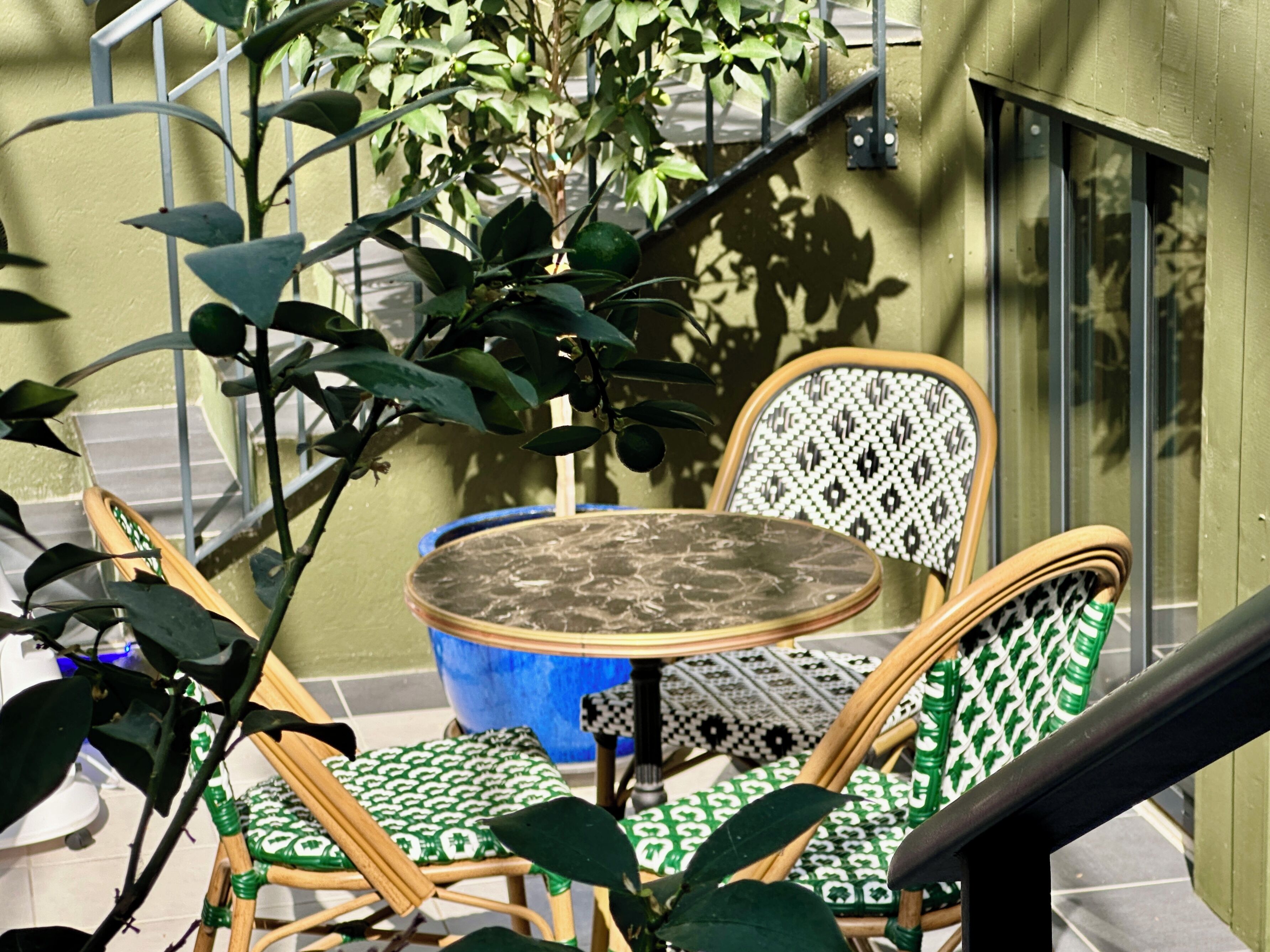 Un petit espace extérieur aménagé avec une table ronde et deux chaises en osier dotées de coussins à motifs.
