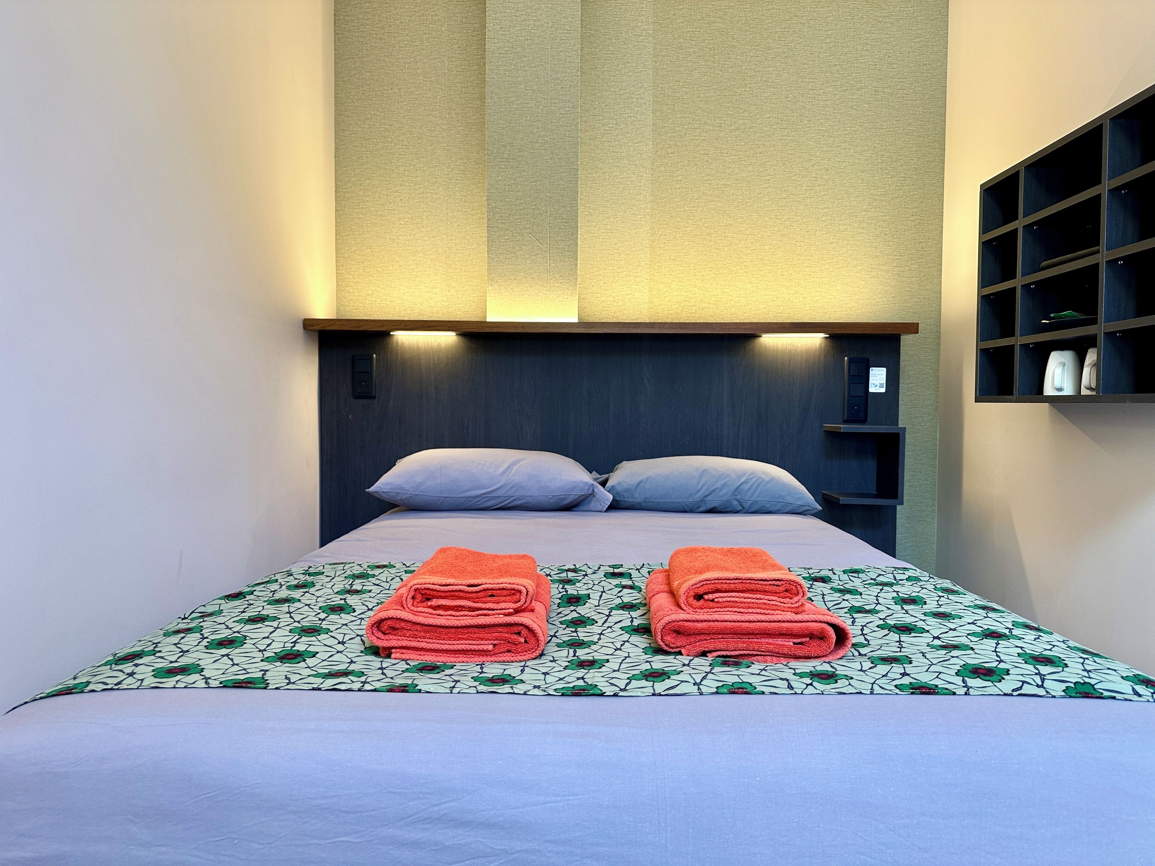 A neatly made bed with a patterned bedspread and two rolled towels on the bed.