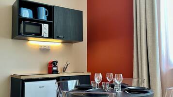 Une cuisine compacte équipée d’un four à micro-ondes, d’une bouilloire et d’une machine à café, un coin repas avec une table pour deux personnes, et un mur d’accent de couleur rouge.
