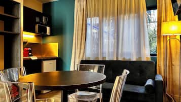 Un salon moderne avec une table ronde, des chaises transparentes, un canapé, une machine à café, un four à micro-ondes et une fenêtre avec des rideaux.