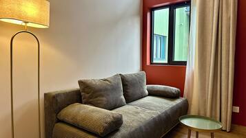 Een woonkamer met een bank, een vloerlamp, een bijzettafeltje en een raam met gordijnen.