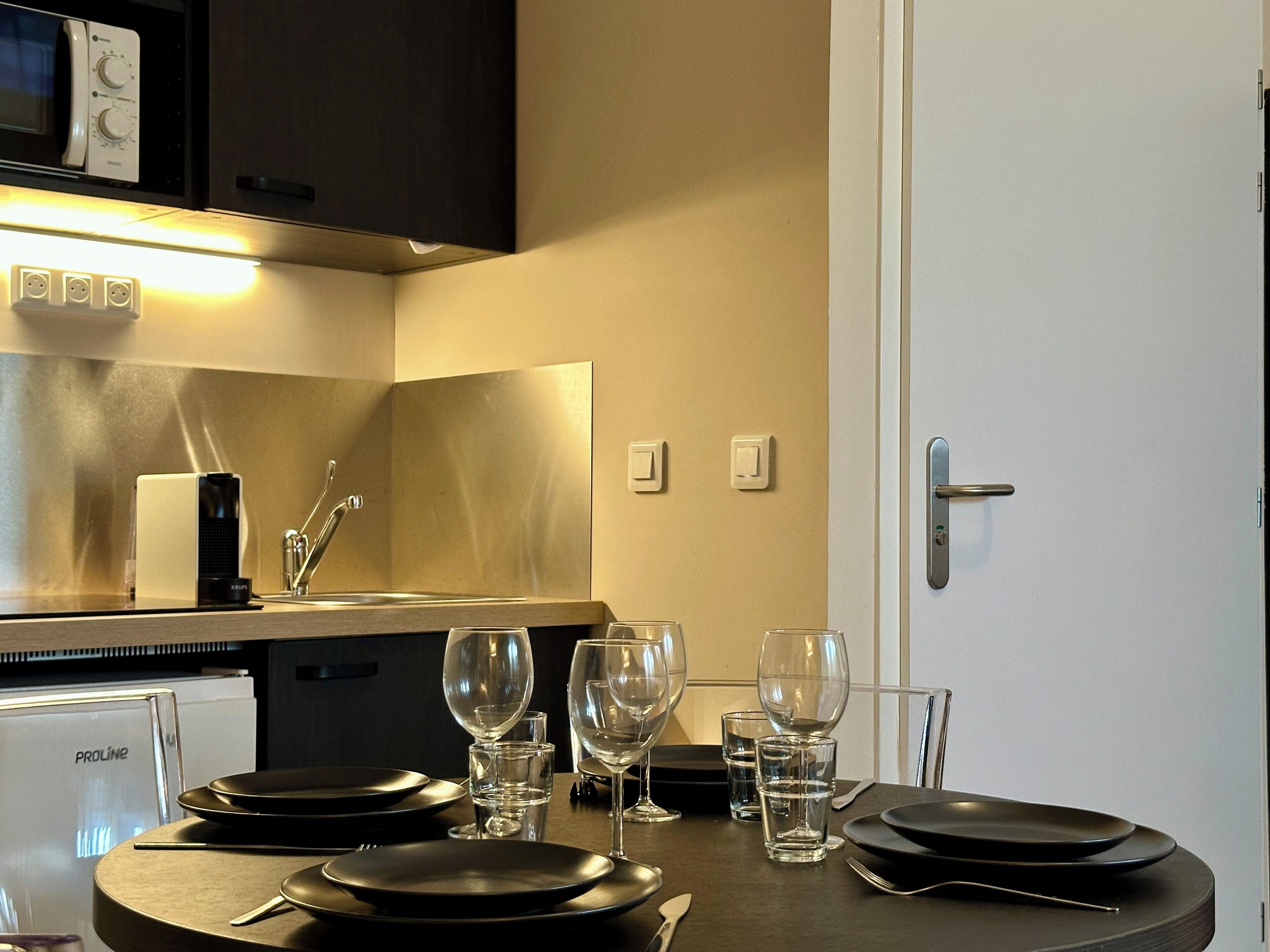Una cocina moderna con microondas, estufa y lavabo. Hay tres copas de vino y platos en la encimera.