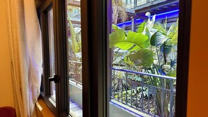 Vista a través de una ventana con barandilla metálica, balcón y abundante vegetación.