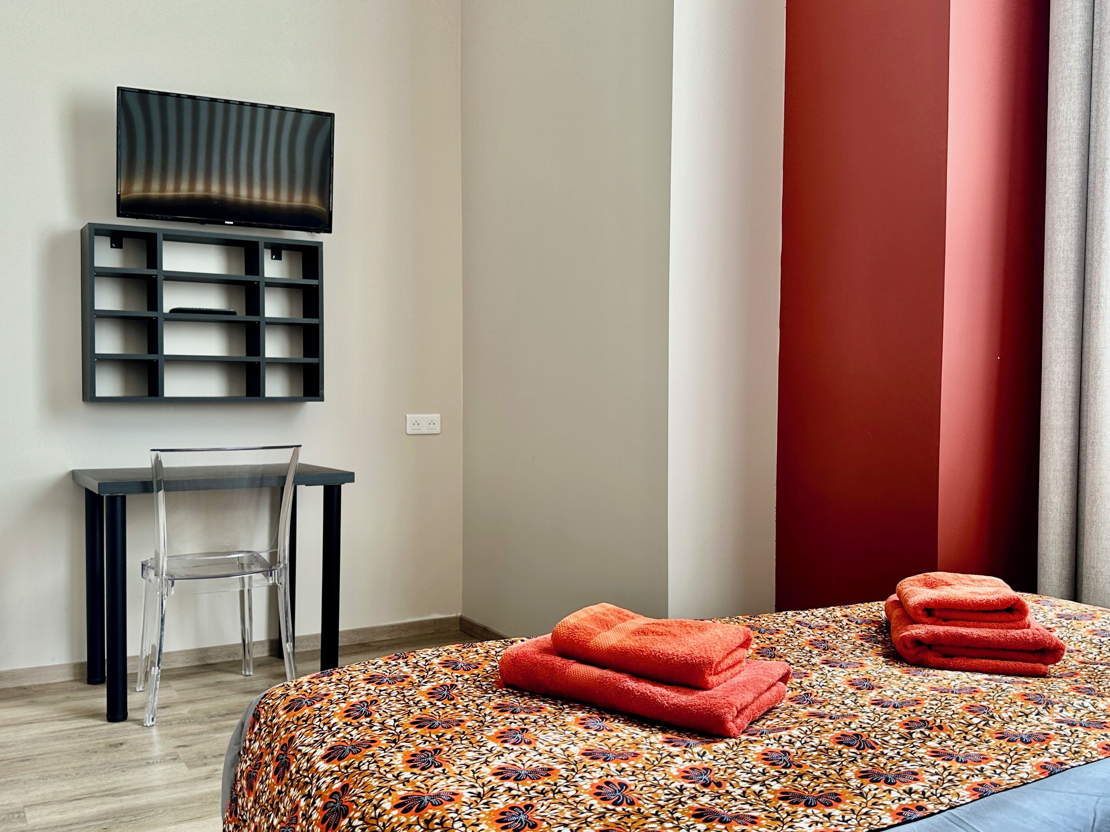 Una camera d'albergo con un letto, una TV a parete, una scrivania e una sedia.