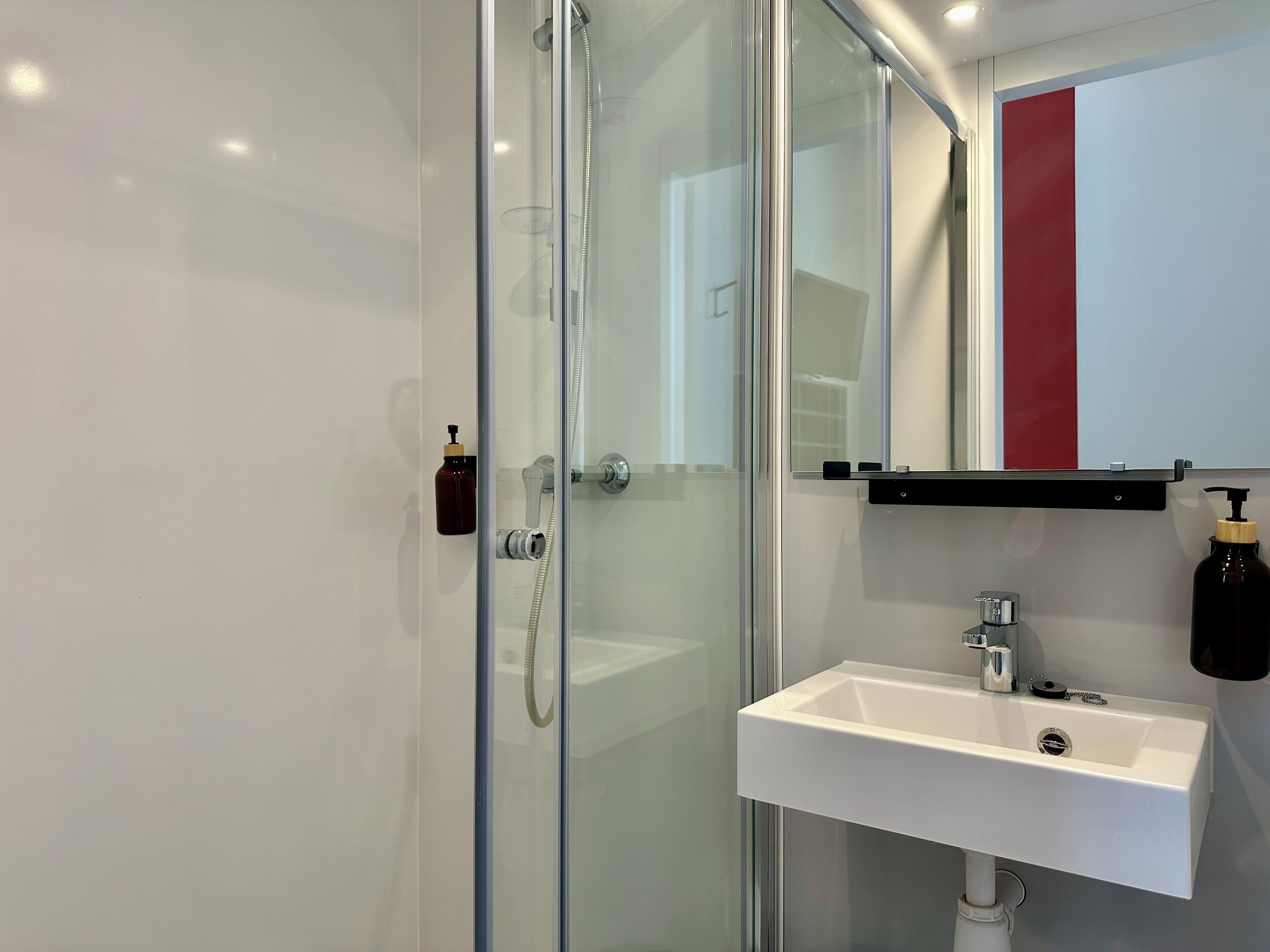 A modern bathroom with a glass shower enclosure, a white sink with a chrome faucet, and a red and white towel rack.