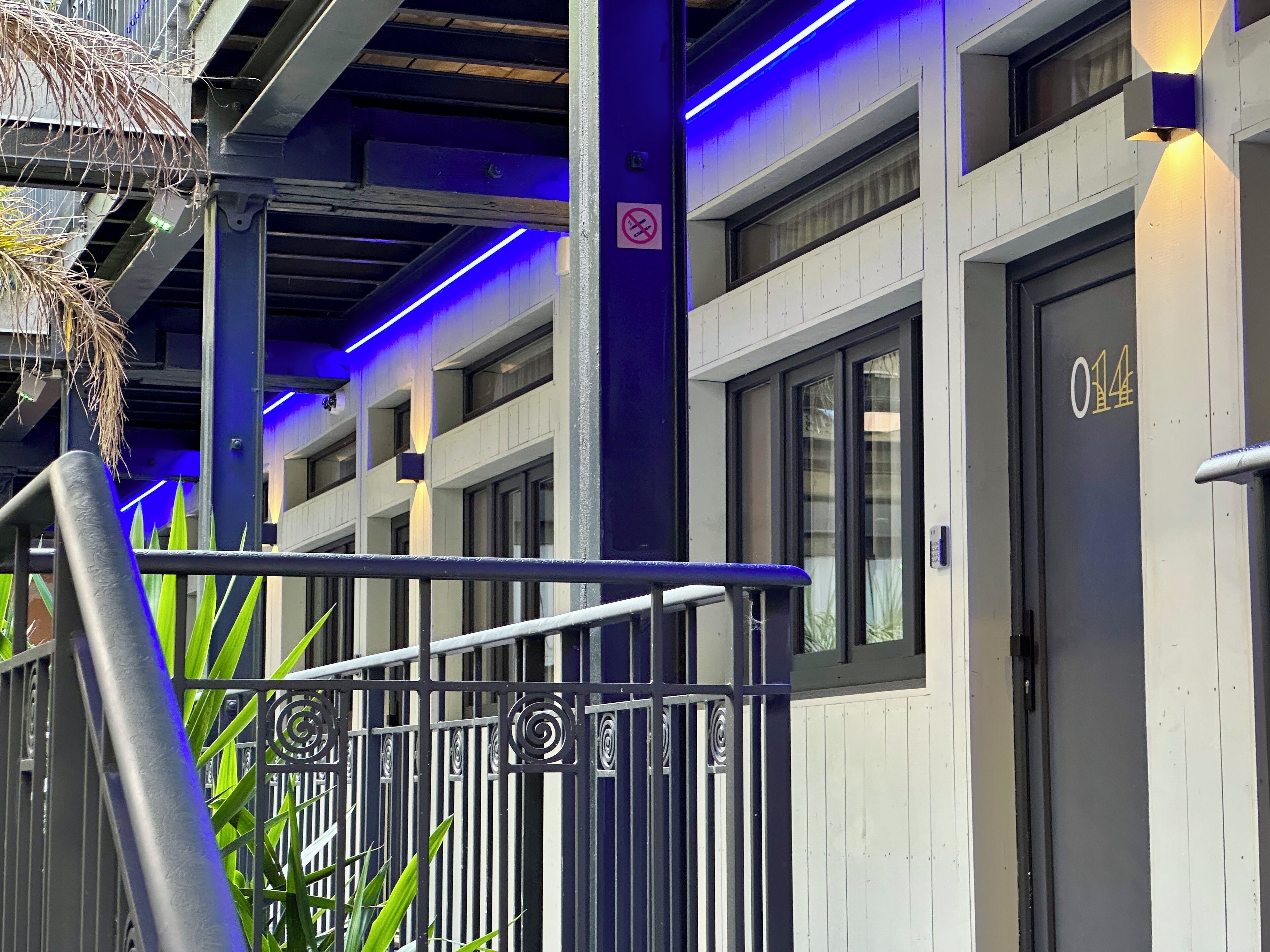 A hotel entrance with a metal gate, a no-smoking sign, and a building with multiple windows and doors.