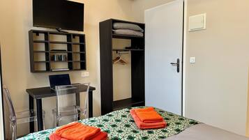 A bedroom with a bed, a desk, a TV, and a wardrobe.