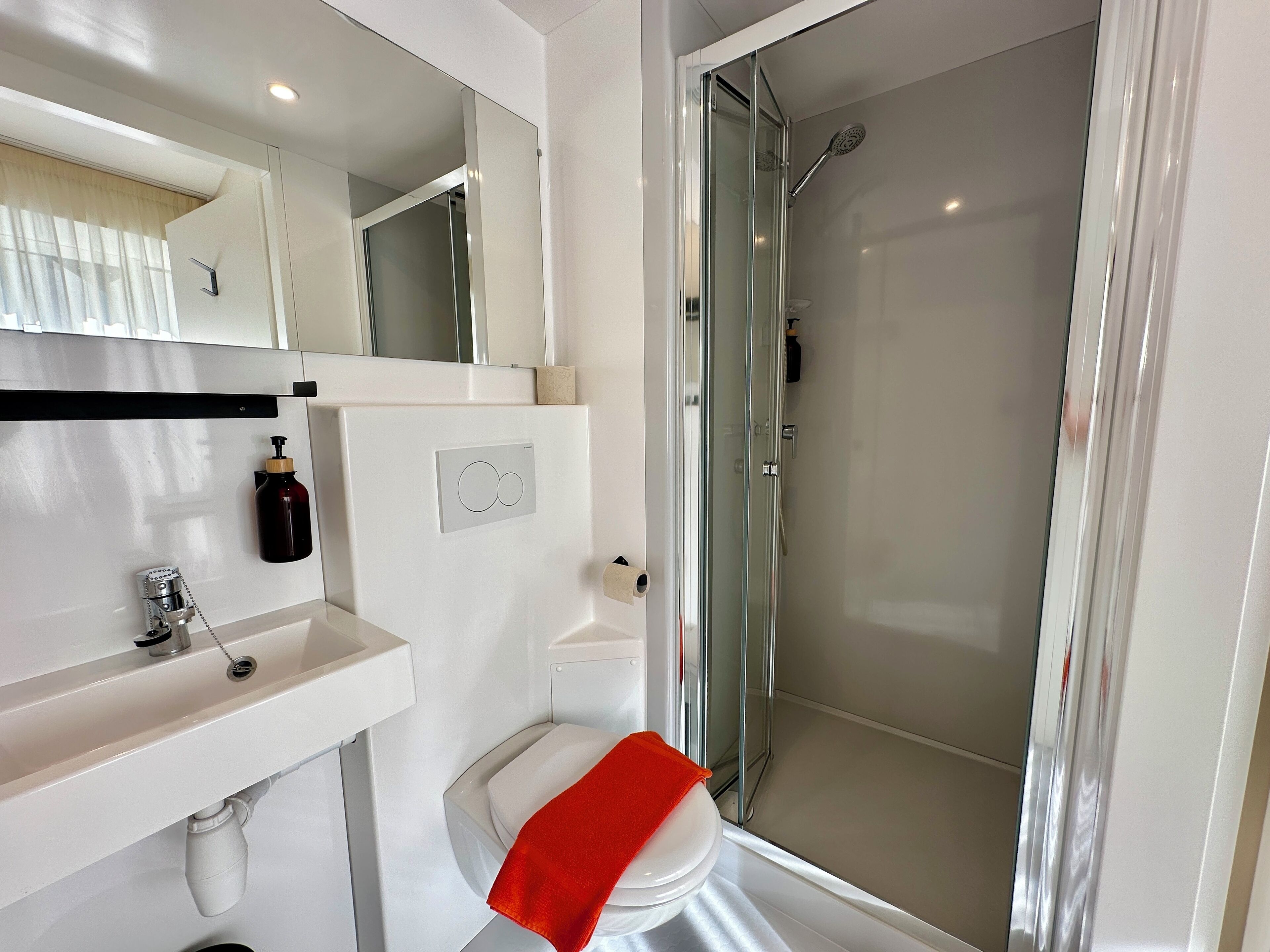 A modern bathroom with a white sink, a toilet, a glass shower enclosure, and a mirror above the sink.
