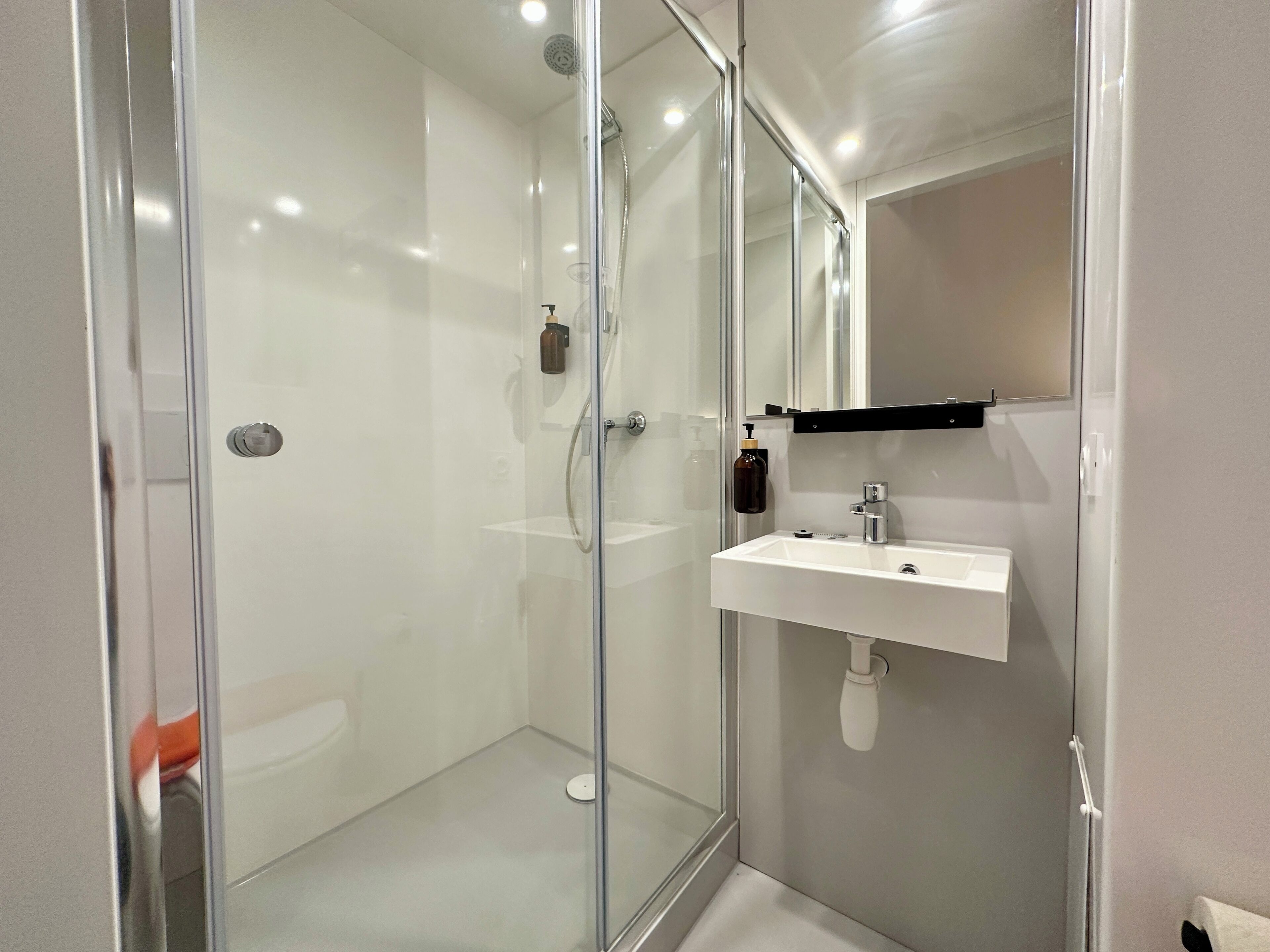 Un baño moderno con cabina de ducha de vidrio, un lavabo blanco y un espejo sobre él.