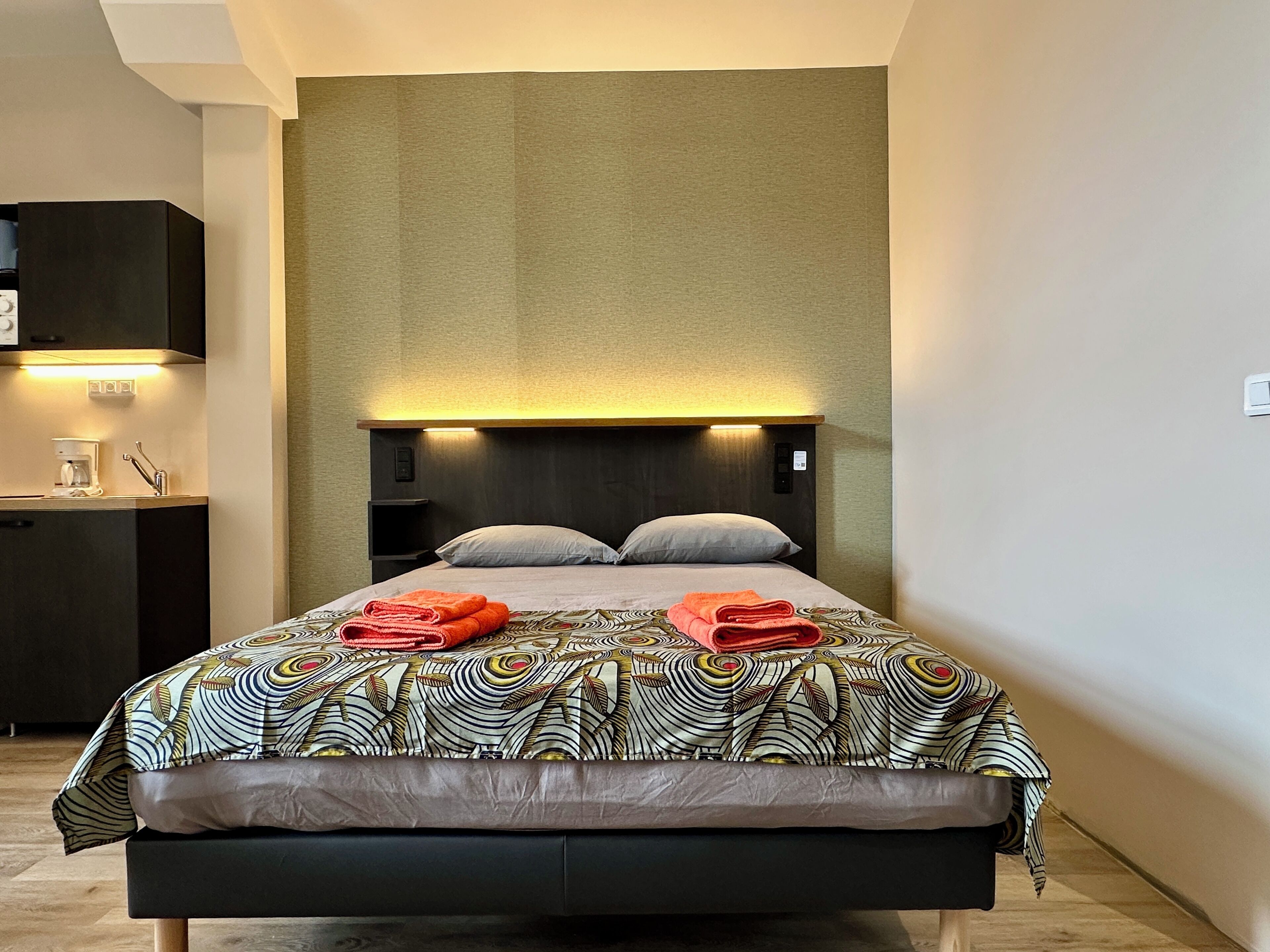 A modern hotel room with a large bed, a bedside table with a lamp, and a built-in wardrobe.
