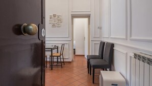A hallway with a dark door, a tiled floor, a small table with a chair, and a radiator. - JOIVY Flats Next To Fontana di Trevi (Rome)