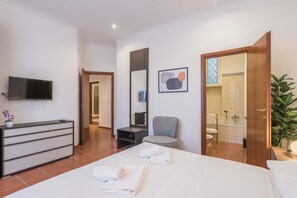 Hotellihuone, jossa on sänky, televisio, työpöytä, tuoli, kylpyhuone ja kasvi.