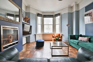 A modern living room with a fireplace, a large mirror, a green sofa, and a coffee table. - 4 Bed House with Pool Table & Parking (Cardiff)