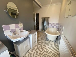 A bathroom with a large oval mirror, two sinks, a bathtub, and patterned floor tiles. - Welsh Retreat With Stunning Views, Sleeps Upto 4 (Mountain Ash)